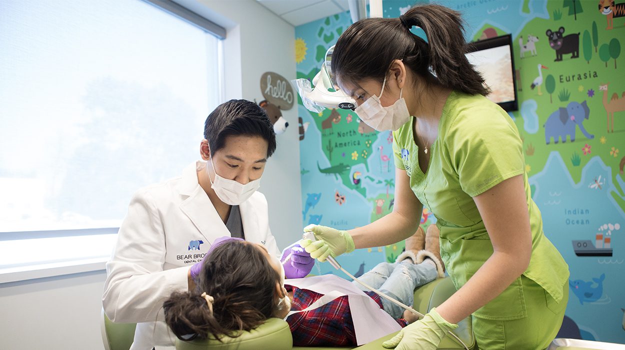 Image shows Dr. Tommy conducting a pediatric dental exam.